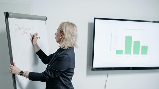 Professional woman in office writing on whiteboard during a business presentation.