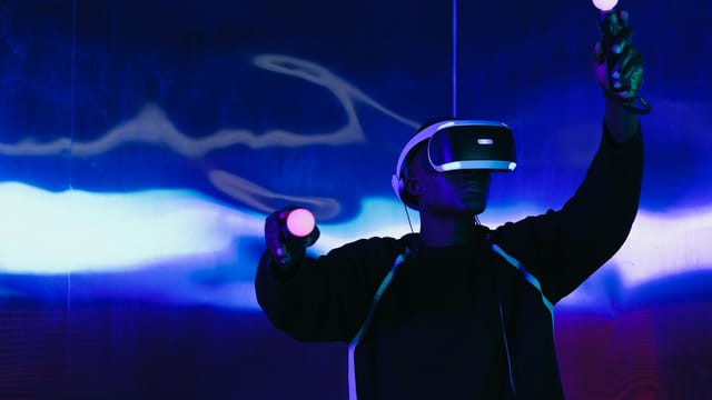 An adult male uses a VR headset and controllers in a futuristic setting with blue lighting.