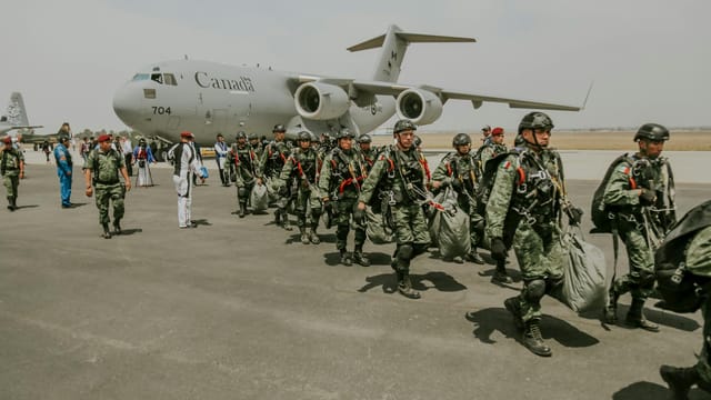 Canadian military paratroopers walk past a C-17 Globemaster on a sunny day at an airport.