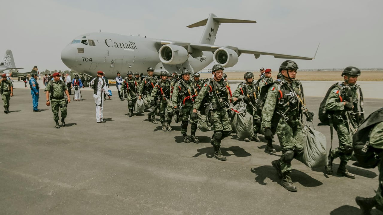 Canadian military paratroopers walk past a C-17 Globemaster on a sunny day at an airport.