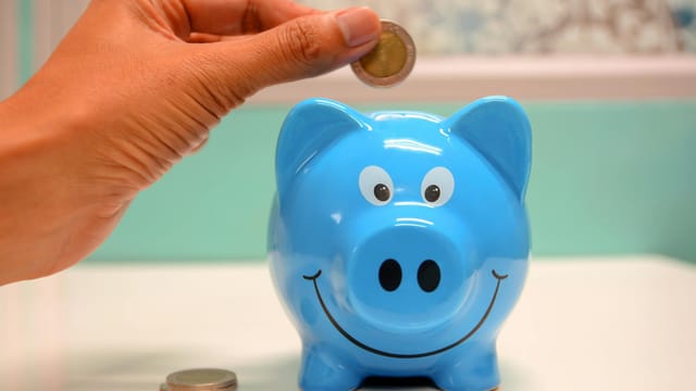 Hand inserting a coin into a blue piggy bank for savings and money management.