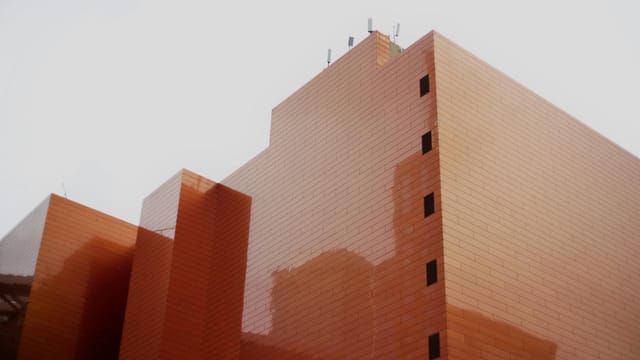 Low-angle view of a modern orange building with antennas against a gray sky in Shanghai.
