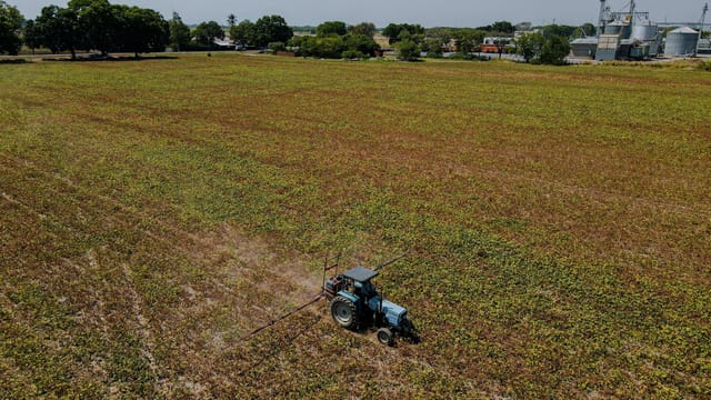 Aerial view of a tractor operating in a large farmland under a clear sky, highlighting agricultural activity.