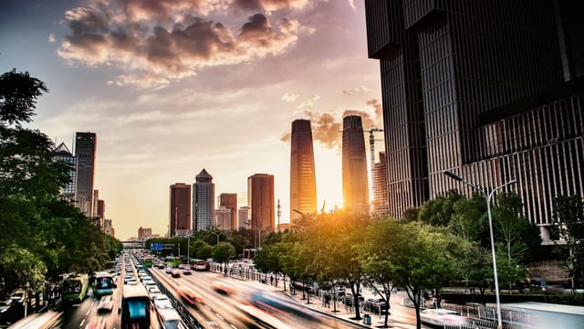 A dynamic view of Beijing's skyline with traffic and skyscrapers at sunset.