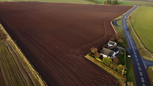 Aerial shot of expansive farmland with a cottage and road in rural Scotland.