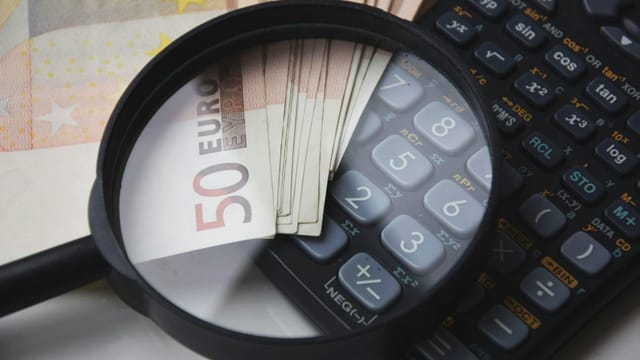 Euro bills under magnifying glass with calculator, symbolizing finance and analysis.
