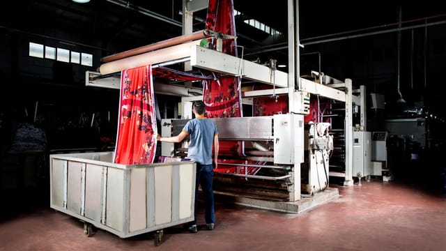 Illustrative image: Worker operates machinery in a textile factory, overseeing fabric production.
