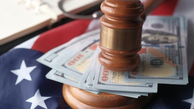 Close-up of a judge's gavel resting on US dollar bills and an American flag, symbolizing justice and finance.