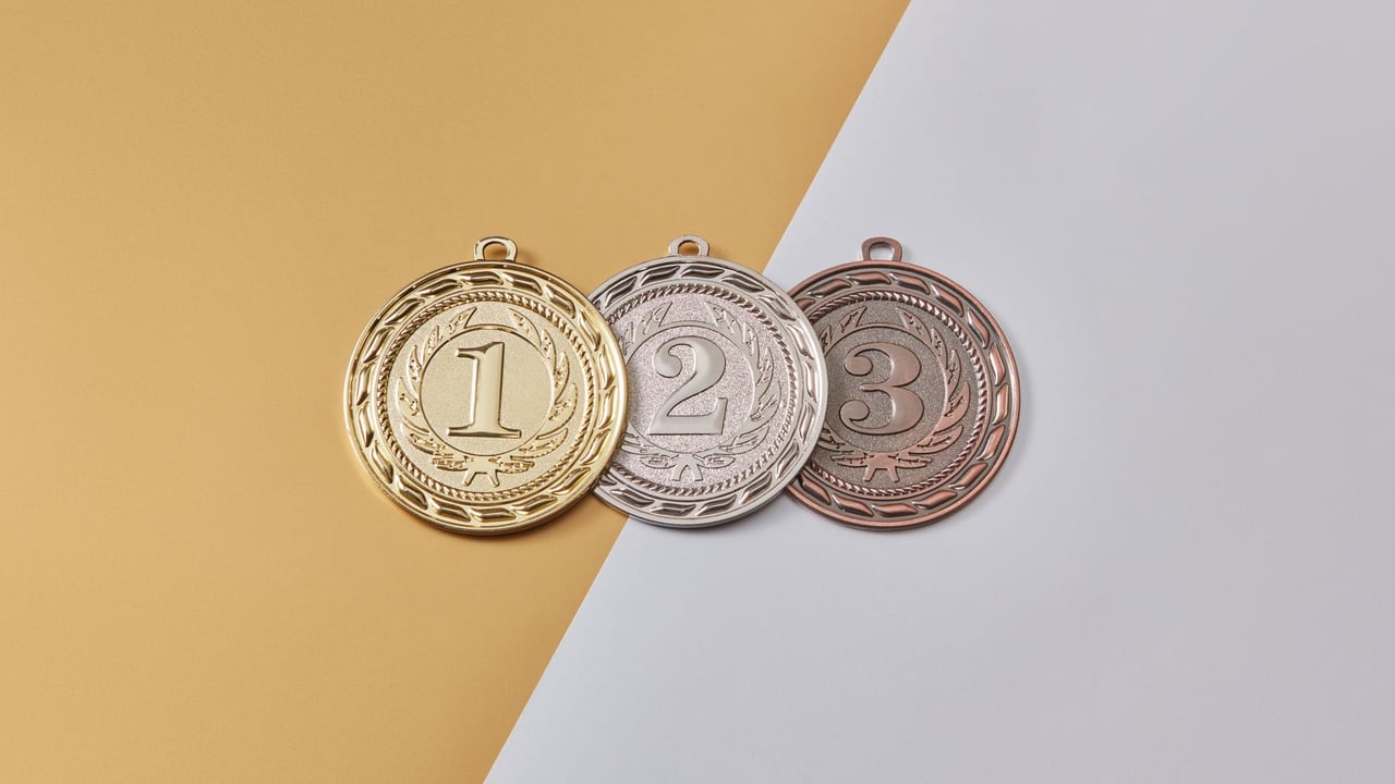 Gold, silver, and bronze medals placed on a modern split-color background, symbolizing achievement.