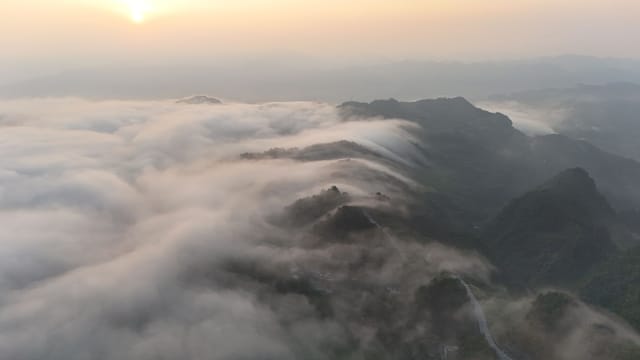 Stunning aerial view of mountains covered in clouds during sunrise, offering a serene and tranquil scene.