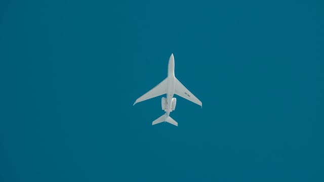 A commercial jet captured mid-flight against a deep blue sky in Dubai.