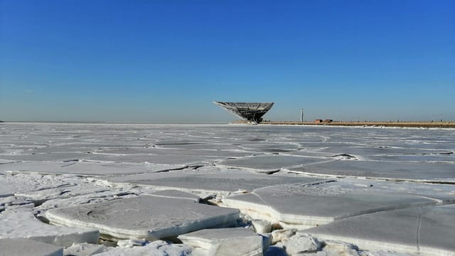 A striking view of a frozen landscape with a modern structure under a blue sky in China.