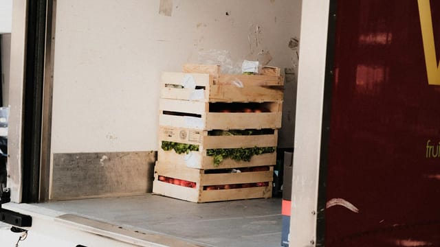 A wooden crate with fresh vegetables loaded inside a delivery truck, ready for transportation.