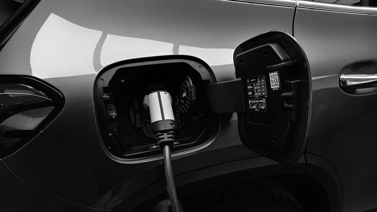Close-up black and white image of an electric vehicle charging at a station.