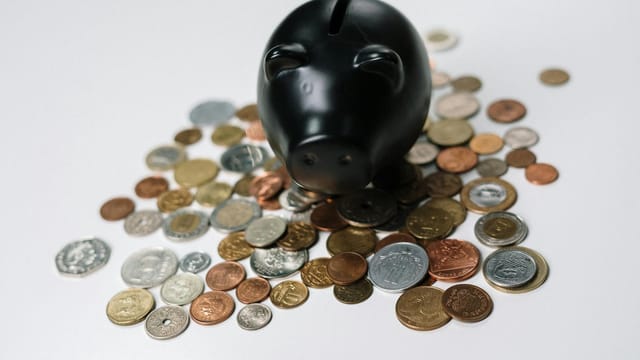 Black piggy bank surrounded by a variety of coins on a white surface, symbolizing savings and finance.