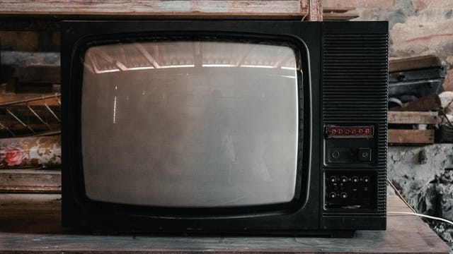 A classic black CRT television in a rustic, workshop environment with a nostalgic vibe.