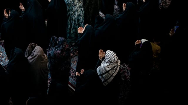 Muslim women in black attire praying during a religious gathering in Karbala, Iraq.