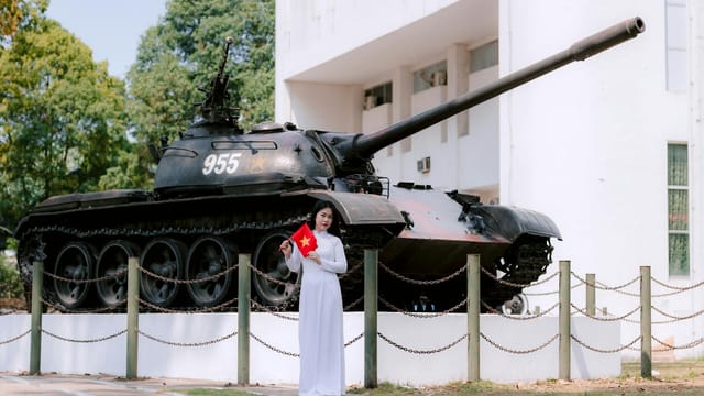 Young woman holding national flag near military tank outdoors, bright day.