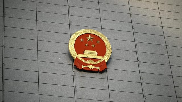 Close-up of the Chinese national emblem on a large concrete building facade, symbolizing government presence.