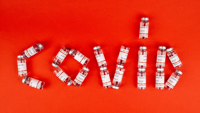 COVID-19 vaccine vials arranged to spell 'COVID' on a red surface.