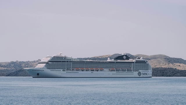 White MSC cruise ship sailing peacefully on the sea against a scenic coastline backdrop.