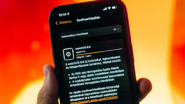 Hand holding a smartphone displaying WatchOS 8.6 update notification against warm gradient background.