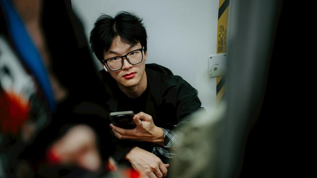 Portrait of a young man holding a smartphone indoors, looking directly at the camera.