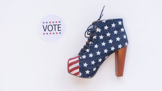 High heel with American flag design beside a voting sticker on white background.