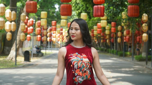 Elegant woman in red dress strolling under vibrant lanterns in summer city park.