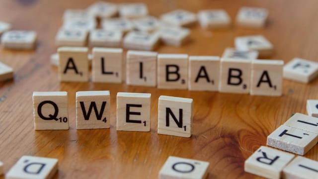 Close-up of Scrabble tiles spelling 'Alibaba' and 'Qwen' on a wooden surface.