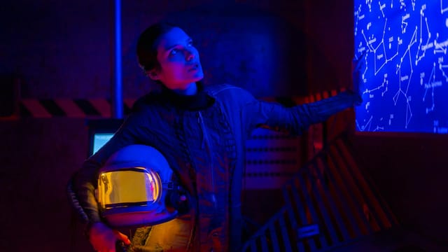 A spacewoman in a futuristic setting examines a star map, holding a space helmet under neon lighting.
