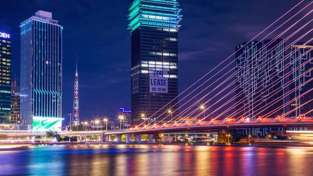 Colorful urban night scene showcasing a brightly lit bridge and modern city skyline reflecting on water.