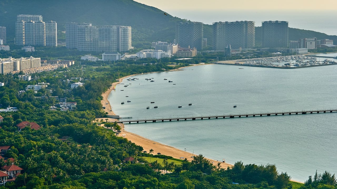 Aerial view of a cityscape with a scenic coastline, buildings, and lush greenery.