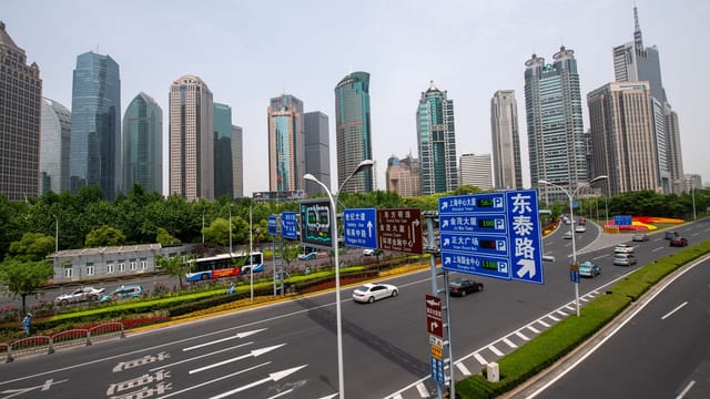 View of Shanghai's modern skyscrapers and highway bustling with traffic under a clear sky.