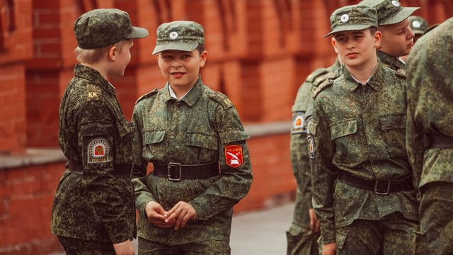 Group of young cadets in camouflage uniforms standing near Moscow's famous red brick architecture.