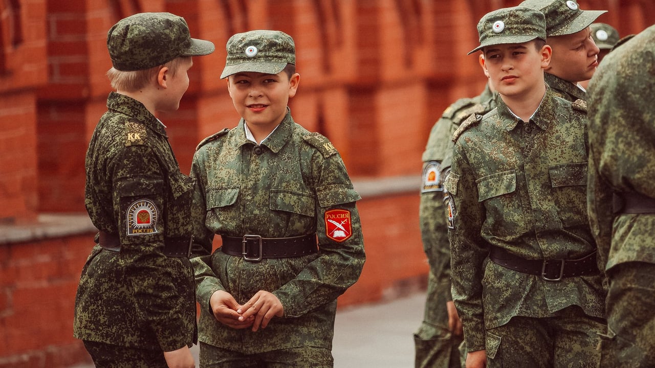 Group of young cadets in camouflage uniforms standing near Moscow's famous red brick architecture.