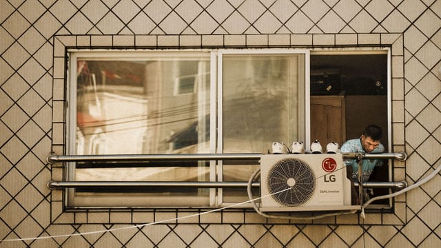 Man looks outside a window with an LG air conditioner unit visible, creating a reflective effect.