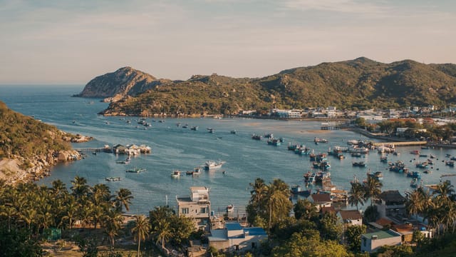 A tranquil view of a Vietnamese fishing village with boats and mountains under a clear sky.