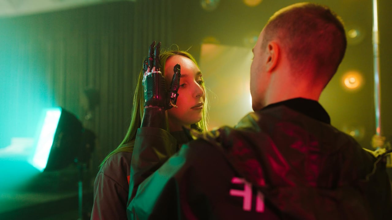A man with a prosthetic hand gently touches a woman's face in a cyberpunk setting.