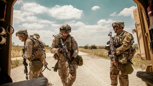 Three soldiers in camouflage gear with rifles in an outdoor military training exercise.