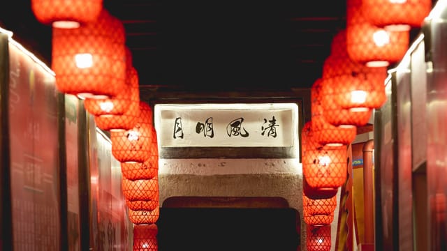 Dimly lit corridor adorned with red lanterns and Chinese calligraphy, creating a warm ambiance.