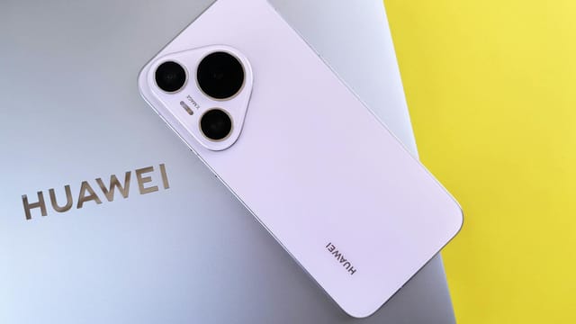 A sleek smartphone with a triple camera setup rests on a laptop, contrasting against a vibrant yellow background.
