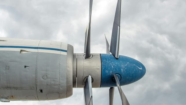 Detailed view of a blue propeller on an aircraft with moody clouds in the background.
