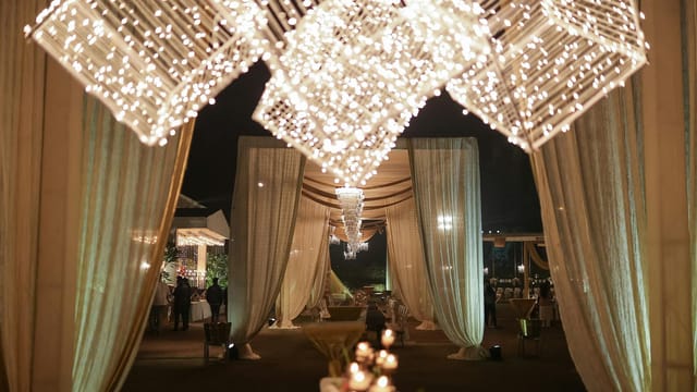 A beautifully lit outdoor event space adorned with fairy lights and draped curtains, creating a magical evening atmosphere.