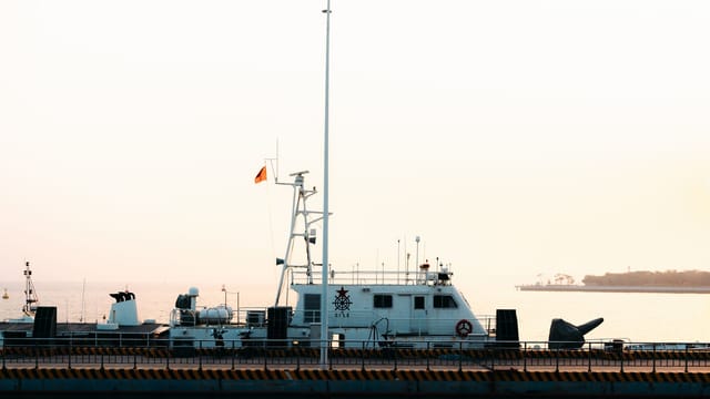 A coast guard ship docked at the harbor during sunrise with a calm sea backdrop.