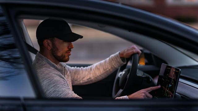 A man interacts with a touchscreen inside an electric car, driving through Dallas, TX.