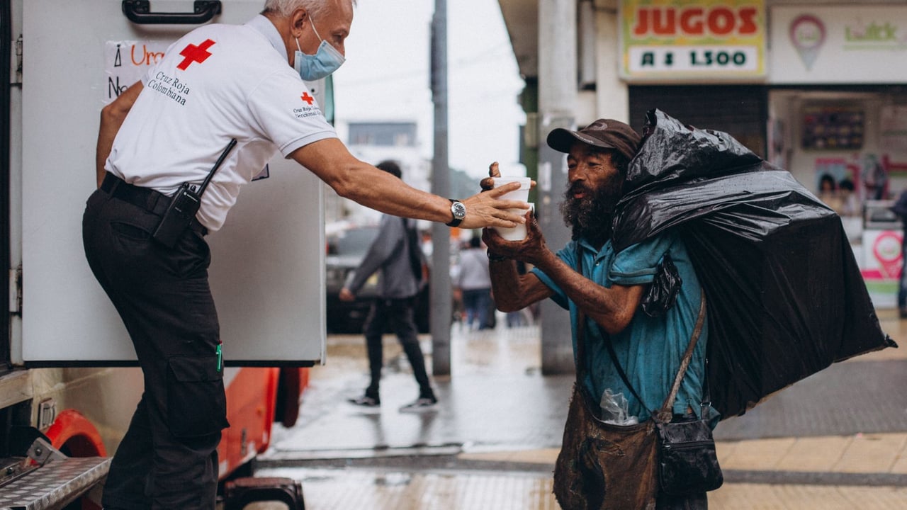 Red Cross worker assisting a homeless man outdoors with kindness.