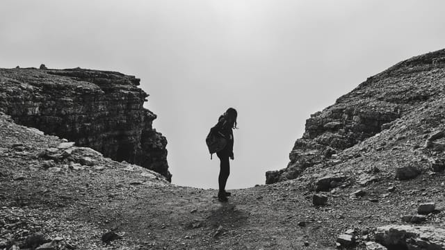 Black and white photo of a woman hiking at Passo Pordoi, capturing a dramatic mountain scene.
