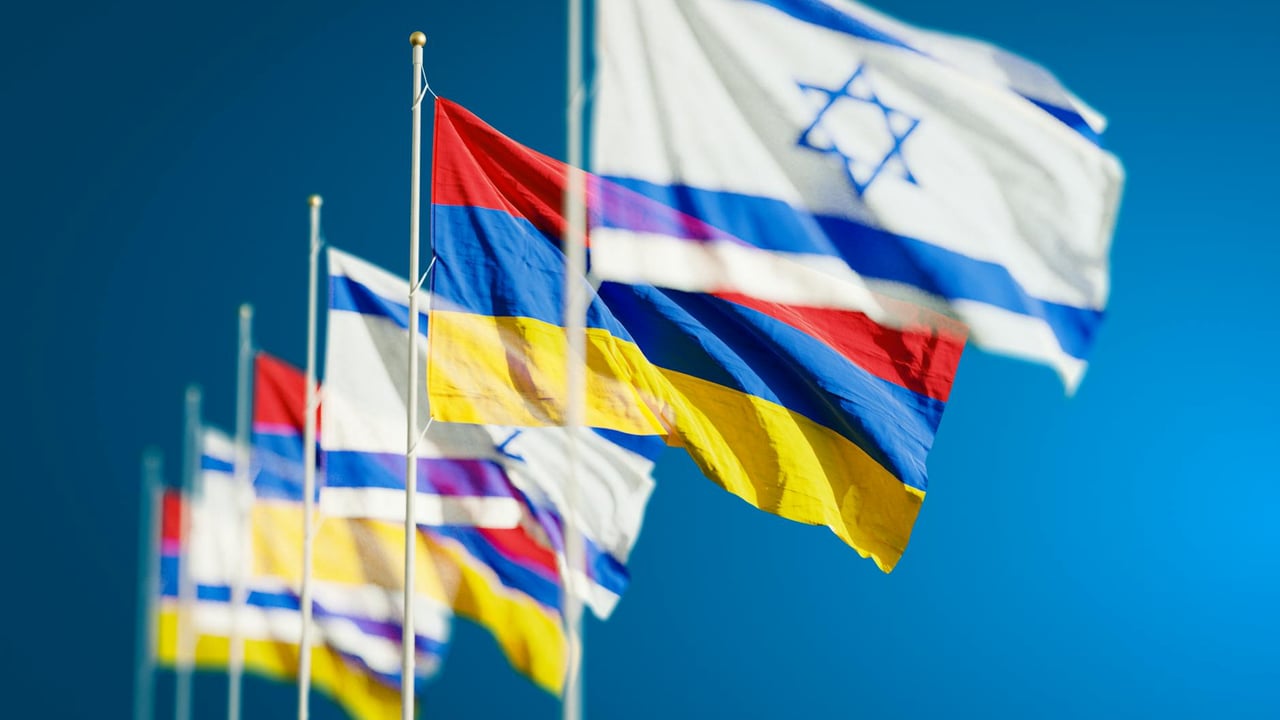 Vibrant national flags of Israel and Armenia waving against a clear blue sky.