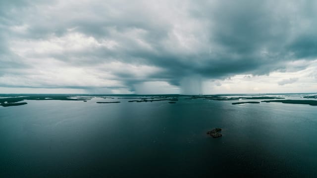 A stunning aerial view of a vast ocean under dramatic cloud formations and rain in the distance.